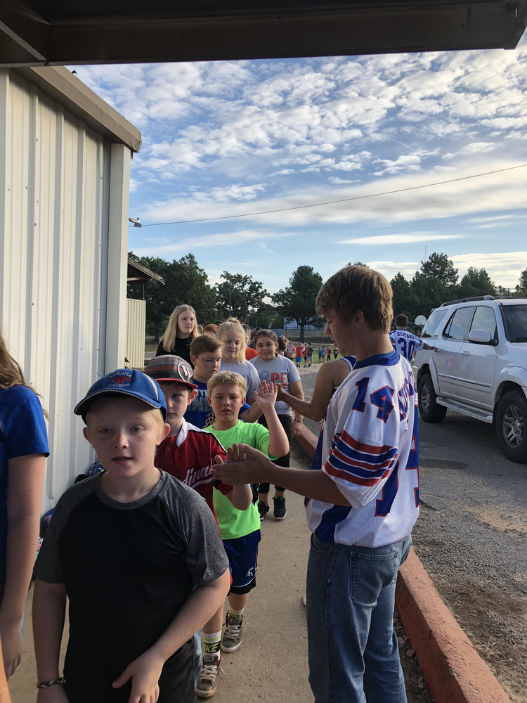 Junior football players and cheerleaders greet students in car rider line